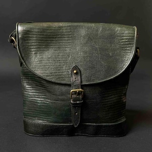 Könnte beinhalten: Dunkelgrüne Leder-Umhängetasche mit einem strukturierten, reptilienartigen Muster. Die Tasche hat einen Klappenverschluss, der mit einer Schnalle gesichert ist, und einen Schulterriemen. Die Tasche ist etwa 30 cm breit und 25 cm hoch.