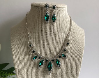 May include: A silver necklace and earrings set with emerald green crystal stones. The necklace features a cascading design with multiple teardrop-shaped stones.