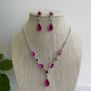 Pu&ograve; includere: Un set di collana e orecchini in argento con cristalli rosa a forma di goccia. La collana ha un design a forma di Y con cristalli pi&ugrave; piccoli lungo la catena.