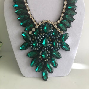 May include: A statement necklace with a large, emerald green, crystal design. The necklace is made of faceted, teardrop-shaped crystals arranged in a cascading pattern.