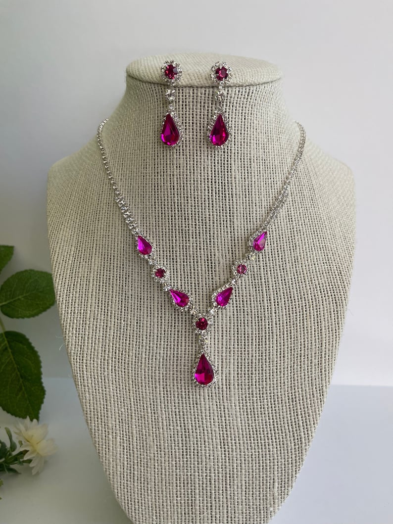 Pu&ograve; includere: Un set di collana e orecchini in argento con cristalli rosa a forma di goccia. La collana ha un design a forma di Y con cristalli pi&ugrave; piccoli lungo la catena.