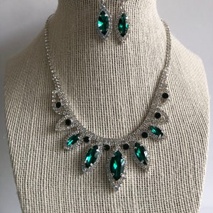 May include: A silver necklace and earrings set with emerald green and clear rhinestones. The necklace features a cascading design with multiple emerald green stones.