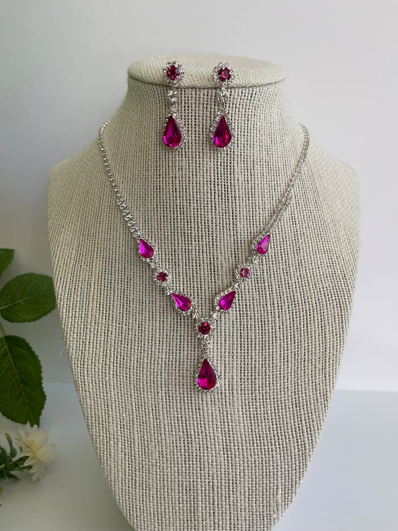 Pu&ograve; includere: Un set di collana e orecchini in argento con strass rosa a forma di goccia. La collana ha un design a forma di Y con strass pi&ugrave; piccoli lungo la catena.