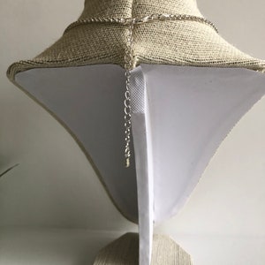 May include: A silver chain necklace with a lobster clasp fastening. The necklace is displayed on a fabric-covered mannequin.