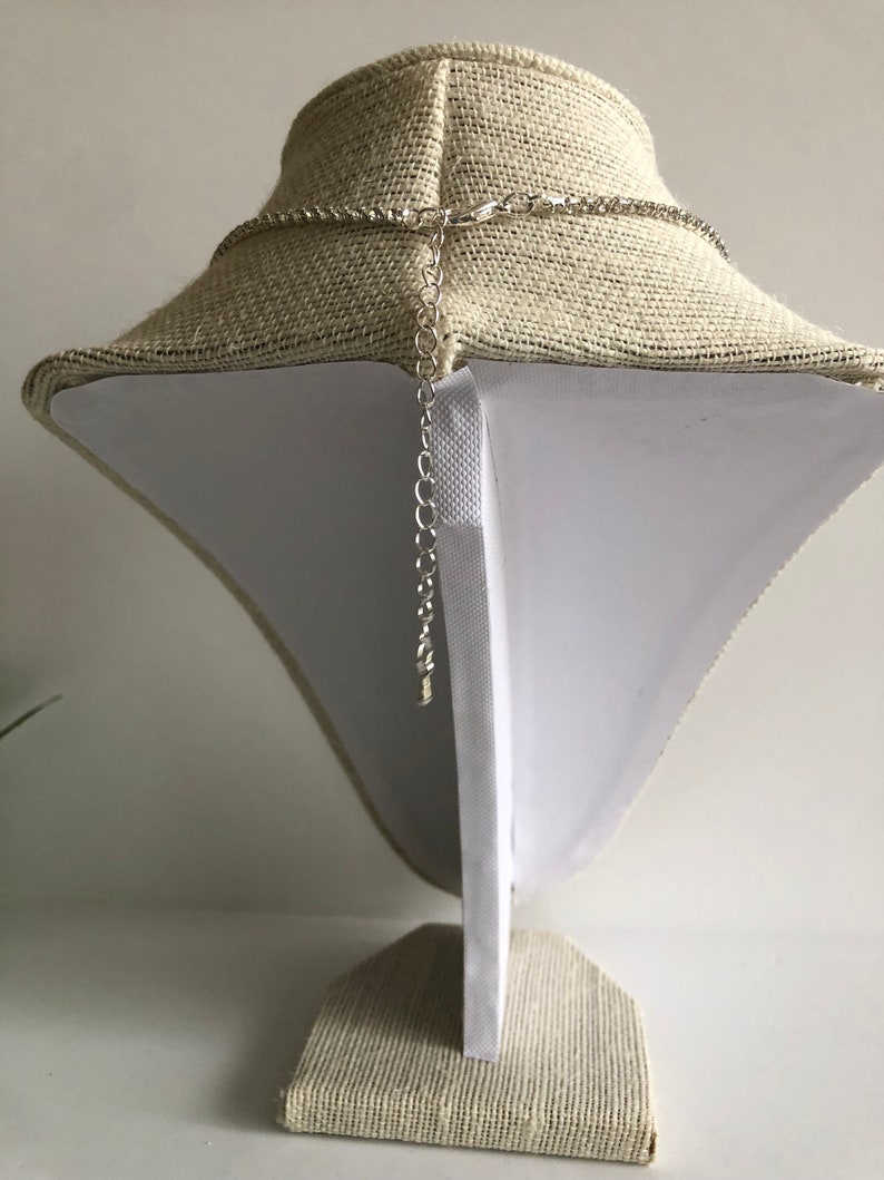 May include: A silver chain necklace with a lobster clasp fastening. The necklace is displayed on a fabric-covered mannequin.