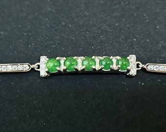 Op de afbeelding: Een zilveren armband met een rij groene jade stenen en heldere zirkonia stenen.