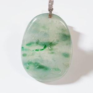 Könnte beinhalten: Ein grüner Jade-Anhänger mit einem geschnitzten Blumenmuster, gefasst in einer silbernen Öse mit kleinen Diamanten.