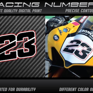 Peut inclure: Numéro de course noir 23 avec un contour rouge sur un fond en fibre de carbone. Le numéro est également affiché sur un carénage de moto jaune avec des accents blancs et noirs. Le texte "Broncos Racing Team" est visible sur le carénage.