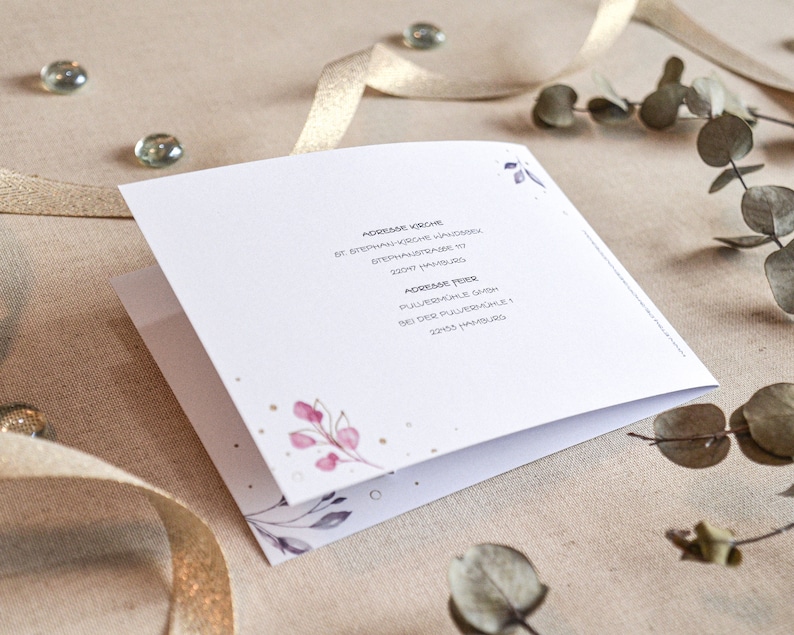 May include: A white card with a floral design and gold accents. The text on the card reads "Adresse Hochzeit" and "Adresse Feier".