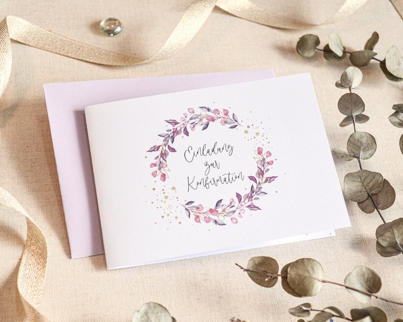 May include: A white card with a purple floral wreath and gold glitter. The text on the card reads "Einladung zur Konfirmation".
