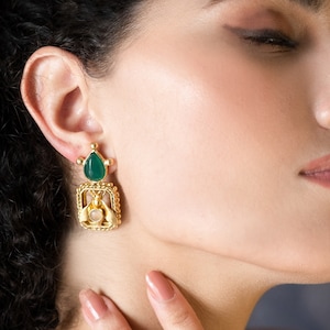 Pode incluir: Um par de brincos de ouro com uma gema verde e uma pedra branca. Os brincos são pendentes e têm um design delicado.