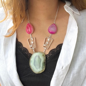 May include: A silver necklace featuring a large green agate pendant and two smaller pink agate drops. The necklace has a delicate silver chain and intricate wirework.