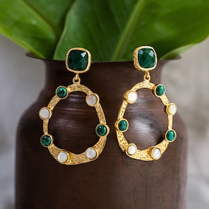 Puede incluir: Pendientes de aro de oro con piedras verdes y blancas. Los pendientes tienen un diseño de metal texturizado y martillado.