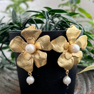 May include: Gold flower-shaped earrings with a pearl in the center of each flower and a dangling pearl on each earring.