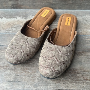 May include: A pair of brown and beige patterned slippers with the text "THE ENACHE" on the insole.