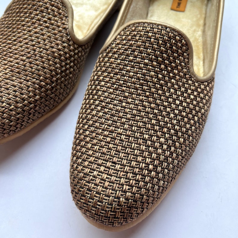 Op de afbeelding: Een paar gouden geweven pantoffels met een zachte, pluche voering. De pantoffels hebben een geweven patroon en een spitse neus.
