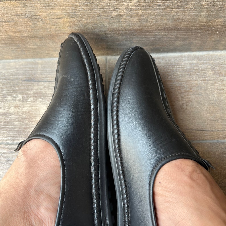 Op de afbeelding: Een paar zwarte leren instappers. De schoenen hebben een ronde neus en een decoratieve gestikte rand langs de randen. De schoenen worden van bovenaf getoond.