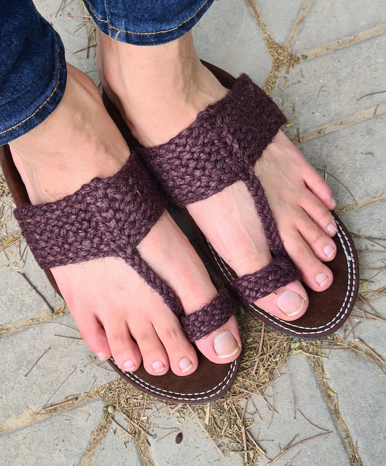 May include: A pair of brown leather sandals with a woven strap design. The sandals are worn on a person's feet.