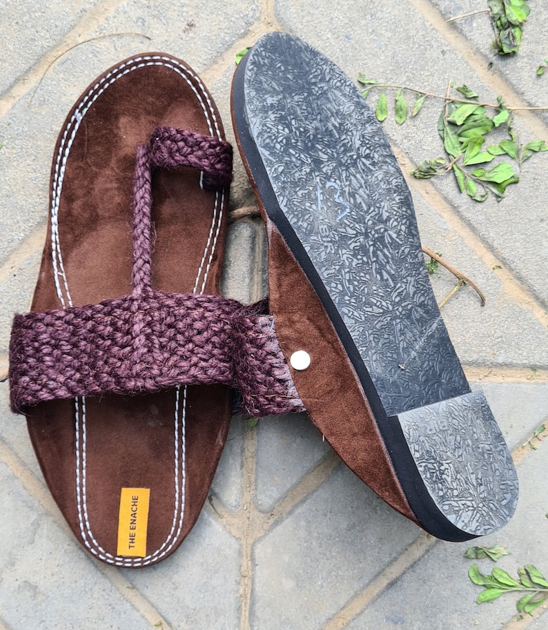 May include: Brown leather sandals with a woven strap and a rubber sole. The sandals have a toe loop and the brand name "THE ENACHE" is printed on the sole.