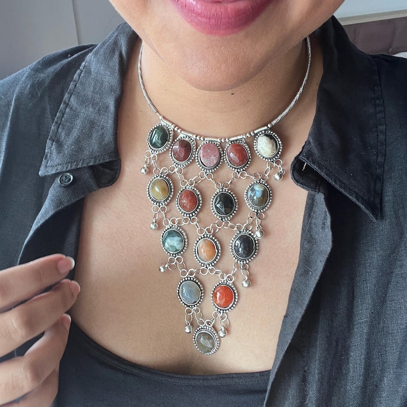 May include: Silver-toned necklace featuring a cascade of colorful, round gemstones. The necklace has a delicate chain and intricate metalwork, with a variety of stone colors including green, red, pink, and orange. Small dangling accents add movement to the design.