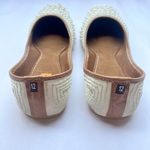 May include: A pair of white flat shoes with pearl embellishments. The shoes have a brown leather lining and are size 12.