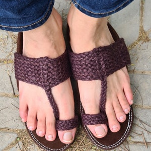 May include: A pair of brown leather sandals with a woven strap design. The sandals have a toe loop and are worn on a person's feet.