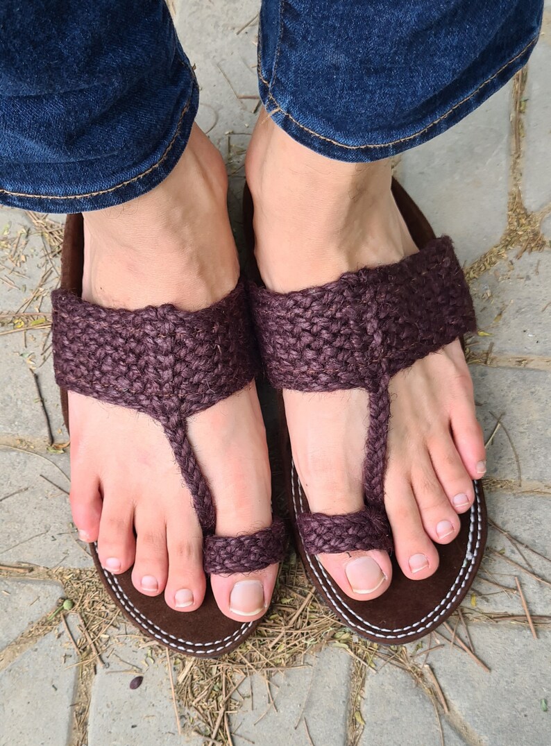 May include: A pair of brown leather sandals with a woven strap design. The sandals have a toe loop and are worn on a person's feet.