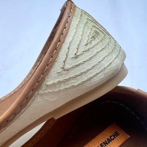 May include: Close-up of a pair of beige ballet flats with brown leather trim and a decorative stitched pattern on the toe. The brand name "ENACHE" is visible on the sole.