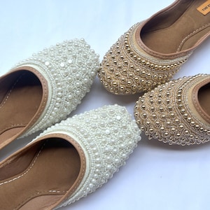 May include: Two pairs of flat shoes with beaded embellishments. One pair is white with white beads and the other pair is brown with gold beads.