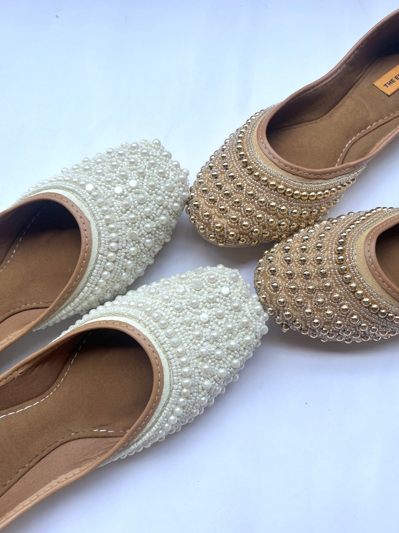 May include: Two pairs of flat shoes with beaded embellishments. One pair is white with white beads and the other pair is brown with gold beads.