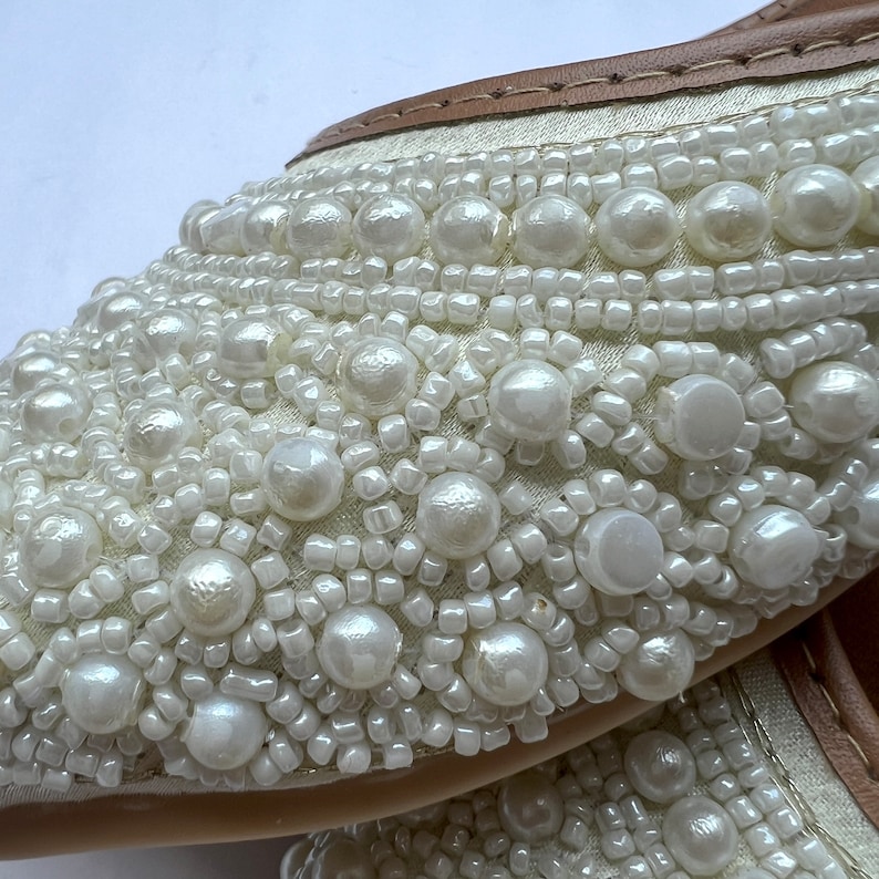 May include: White fabric shoes with a decorative design of white pearls and beads.