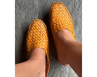 May include: A pair of yellow woven leather sandals with a square toe and an open back.