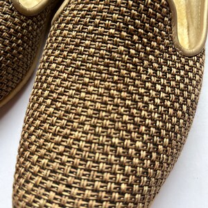 Op de afbeelding: Close-up van een gouden geweven pantoffel met een glad leren hak.