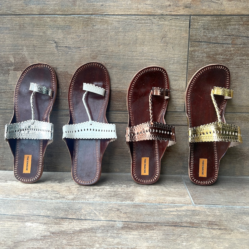 May include: Four pairs of brown leather sandals with decorative straps and toe rings. The sandals have different colored embellishments: white, gold, and copper. The brand name "The  Macabre" is printed on the soles.