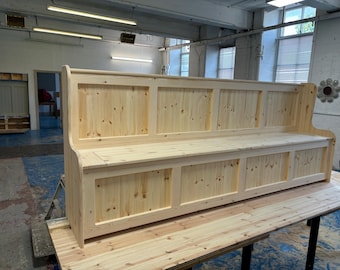 May include: A long wooden bench with a high back and storage compartments underneath. The bench is made of natural wood and has a simple, rustic design.