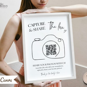 May include: A white sign with a black outline of a camera with a QR code inside. The text on the sign reads "Capture the love & Share" and "Share your photos with us! Scan this QR code with your smartphone, upload & share your favorite photos! Thank you, Emily & Eric".