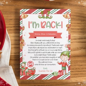Op de afbeelding: Een rood-groen gestreepte kaart met een aquarel-illustratie van een elf. De kaart luidt "Ik ben terug!" en "Emma, Ethan & Sebastian". De elf houdt een cadeau vast en heeft een spreekballon die zegt "Liefde, Twinkle de Elf".
