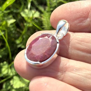 Peut inclure: Pendentif en argent avec une grosse pierre précieuse ovale en rubis. Le rubis est d'un rouge profond et est serti dans une lunette en argent poli. Le pendentif a un design simple et élégant, adapté au quotidien.