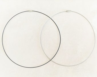 May include: Two necklaces, one black and one silver, are laid out on a white surface. Both necklaces are made of thin, flexible wire.