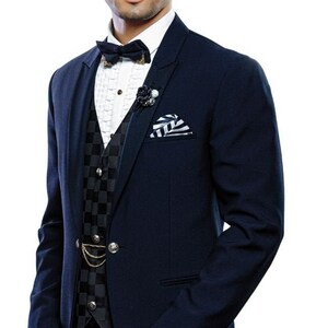 May include: A navy blue suit jacket worn over a white ruffled shirt and a black and gray checkered vest. The ensemble includes a dark navy bow tie, a black lapel flower, a gold chain detail on the vest, and a white and navy striped pocket square.