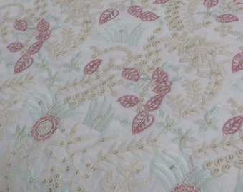Puede incluir: Una tela blanca con bordados intrincados en tonos rosa suave, verde pálido y crema. El diseño consiste en patrones detallados de flores y hojas cosidos por toda la superficie, creando una apariencia texturizada y con capas.
