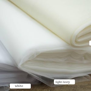 May include: Close-up of three rolls of fabric in white, light ivory, and ivory. The fabric is soft and appears to be tulle or a similar sheer material. The labels identify the colors.