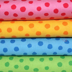 Könnte beinhalten: Nahaufnahme von vier gestapelten Stoffrollen in Rosa, Gelb, Blau und Grün. Jede Rolle weist ein sich wiederholendes Muster aus großen Tupfen in kontrastierenden Farben auf. Der rosa Stoff hat rote Punkte, der gelbe hat orangefarbene, der blaue hat blaue und der grüne hat grüne.