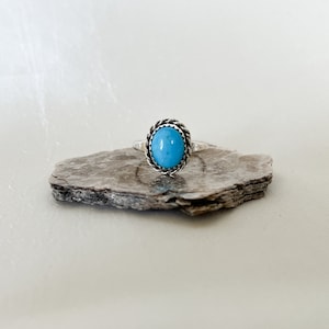 Könnte beinhalten: Ein silberner Ring mit einem blauen Türkis-Stein, der in einem seilartigen Design gefasst ist.