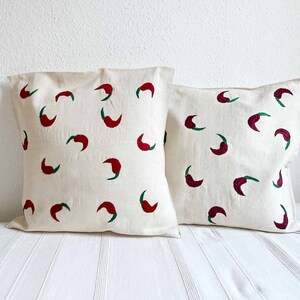 May include: Two white pillow covers with red and green chili pepper designs. The pillows are made of a soft, natural fabric.