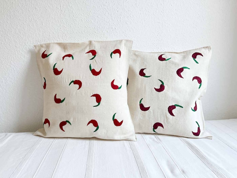 May include: Two white pillow covers with red and green chili pepper designs. The pillows are made of a soft, natural fabric.