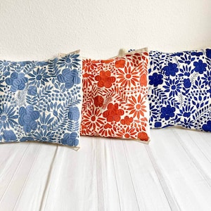 May include: Three embroidered throw pillows with floral patterns. The pillows are white with blue, red, and blue floral designs.