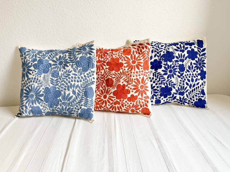 May include: Three embroidered throw pillows with floral patterns. The pillows are white with blue, red, and blue floral designs.