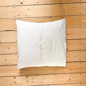 May include: A white pillow with a seam down the center, lying on a wooden floor.