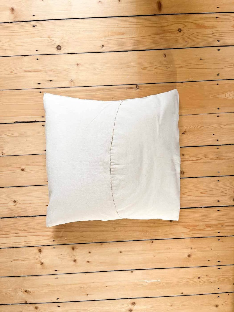 May include: A white pillow with a seam down the center, lying on a wooden floor.